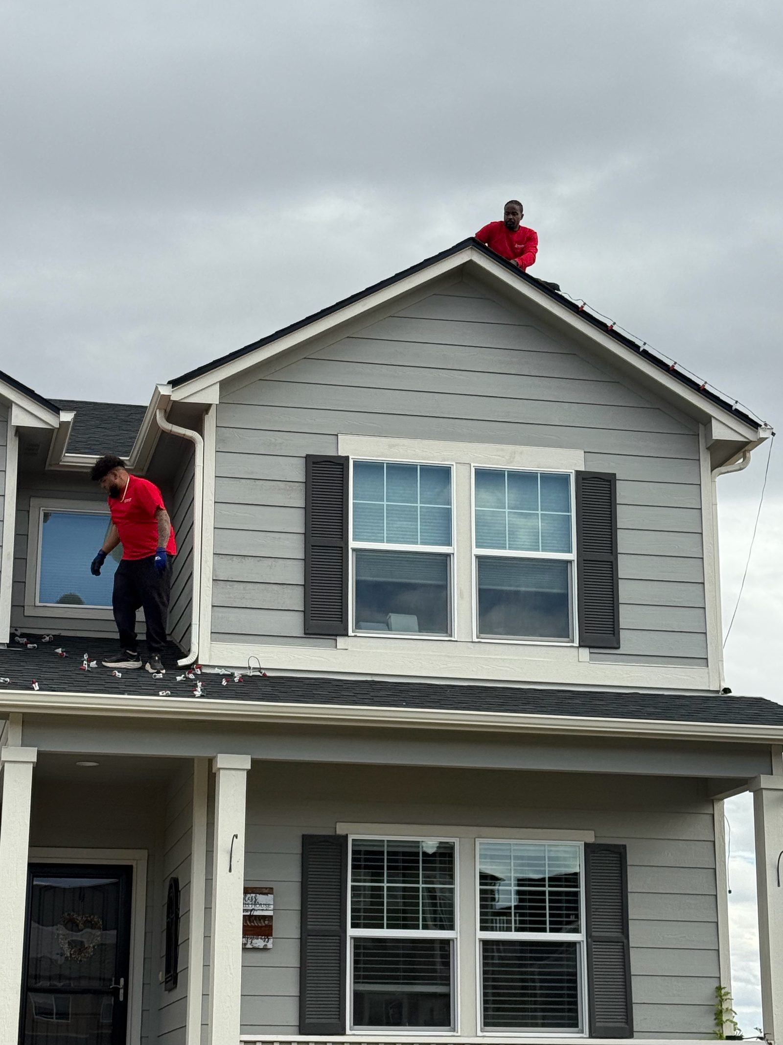 Christmas Lights Colorado Springs installers on roof peak hanging holiday lights on a gray Colorado Springs house