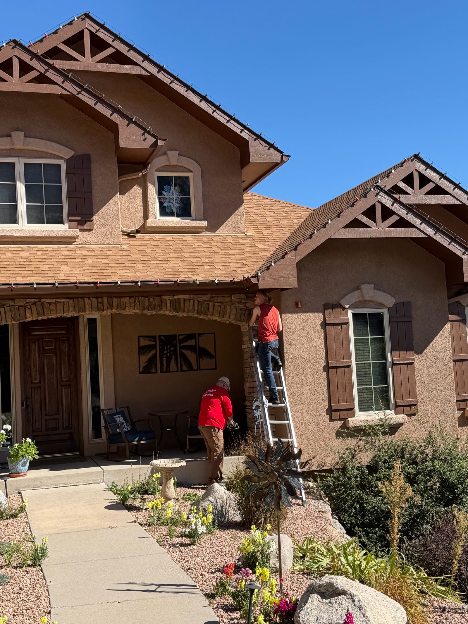 Christmas light installers on ladder hanging red Christmas lights on a Colorado Springs home Christmas light installers on ladder hanging red Christmas lights on a Colorado Springs home