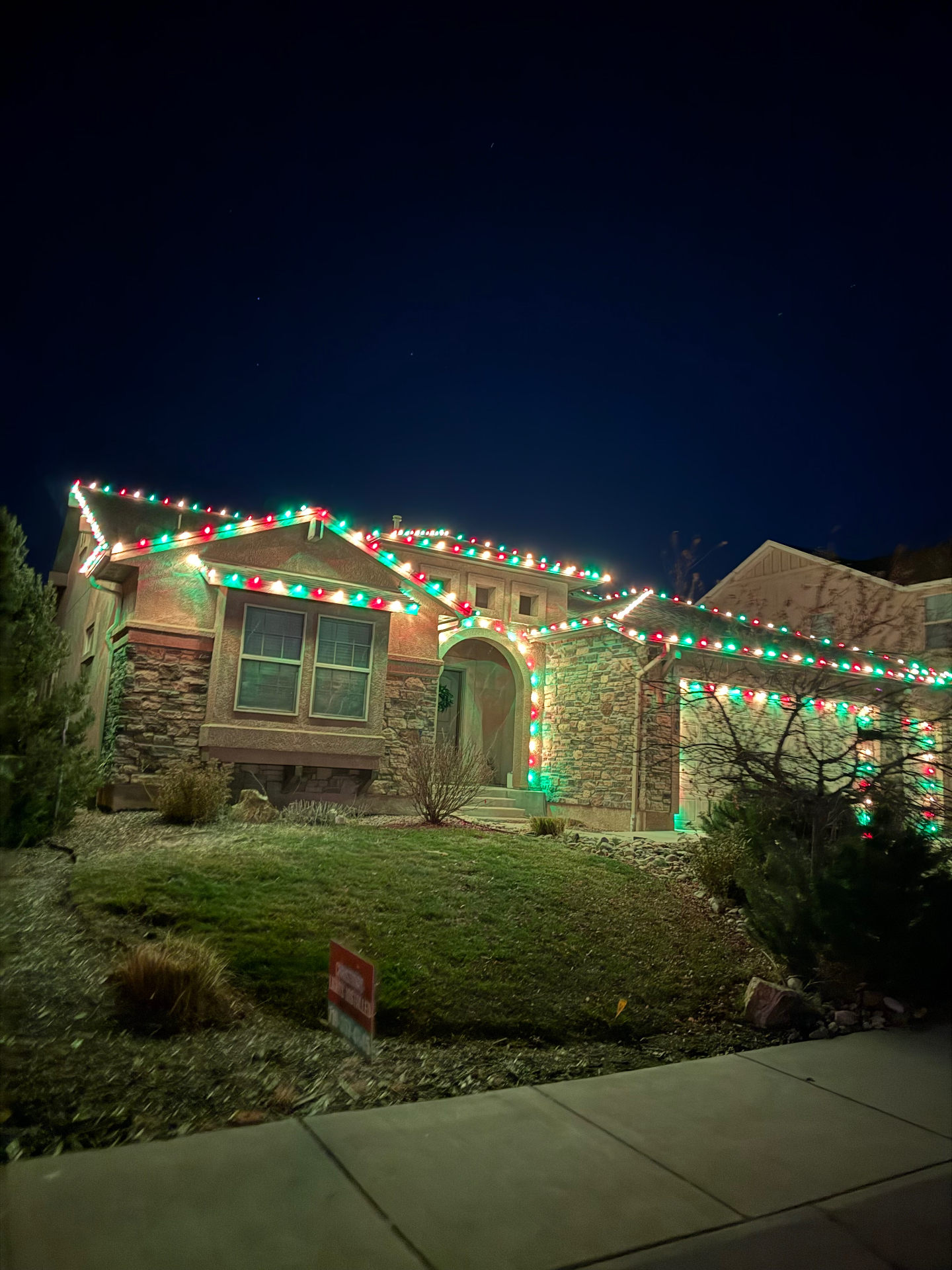 Multicolor Christmas lights on a two-story Colorado Springs home with roofline and landscape holiday lighting